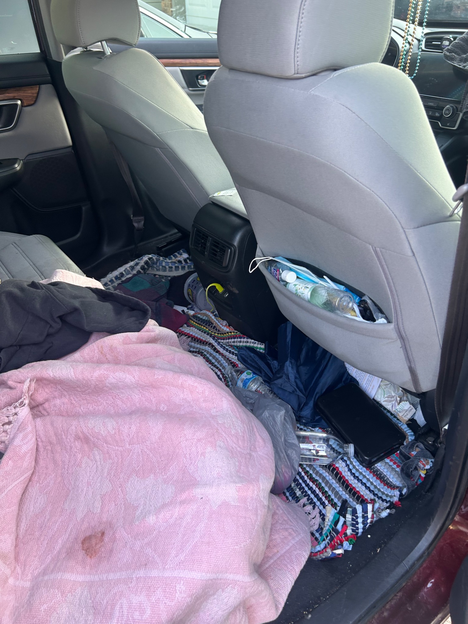 Vehicle rear interior before detailing, with clutter on the seats and floor